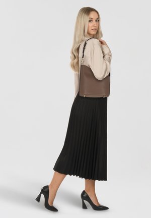 Brown leather shoulder bag with a structured shape, featuring gold hardware and a textured finish, worn with a black pleated skirt and heels.