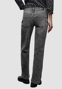 Jean en denim gris avec une coupe droite, comportant deux poches arrière et une texture décolorée. Porté avec des chaussures noires et un pull à motifs.