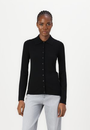 Zwarte lange mouwen gebreide polo met kraag, voorzien van een knoopsluiting aan de voorkant. Materiaal heeft een gladde textuur, gecombineerd met lichtgrijze jeans.