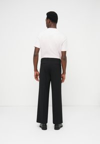 Schwarze Hosen mit weitem Bein und glatter Textur, ausgestattet mit einem taillierten Bund und Gesäßtaschen, kombiniert mit einem hellrosa T-Shirt mit Rundhalsausschnitt.