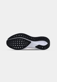 Semelle d'une chaussure de course noire et blanche avec un motif de traction en forme de losange et un petit logo au centre sur un fond uni.