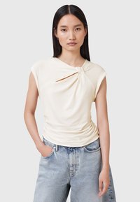 Lichtbeige top met een gedraaide knoopdetail bij de halslijn, korte mouwen en geplooide textuur, gecombineerd met hoog-waisted, licht denim jeans.