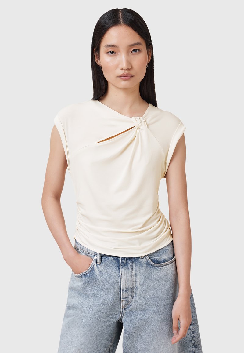 Lichtbeige top met een gedraaide knoopdetail bij de halslijn, korte mouwen en geplooide textuur, gecombineerd met hoog-waisted, licht denim jeans.