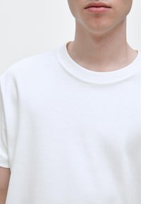 White cotton t-shirt with a crew neck, short sleeves, and a smooth texture. No visible patterns or logos. Simple, minimalistic design.