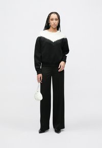 Czarna bluza z białym kołnierzem w kształcie litery V, teksturowanym frędzlem, w połączeniu z czarnymi szerokimi spodniami i małą białą torebką. Czarne buty.