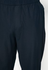 Tamno plave, lagane hlače s elastičnom waist band, s glatkom teksturom i čistim linijama, prikladne za ležerno ili opušteno nošenje.
