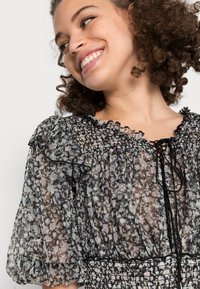 Blusa com estampa floral e mangas curtas bufantes, nas cores preto e pastel. Apresenta corpo franzido com rendinha e detalhe de laço no decote.