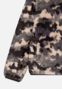 Giacca in finta pelliccia con un motivo camouflage in tonalità di grigio e beige. Texture morbida con orlo e polsini neri.