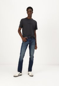 T-shirt à col rond gris foncé avec le logo "Hollister", jean en denim bleu et baskets blanches avec des accents noirs ; coupe décontractée, design épuré.