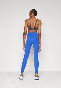 Grå sportsbh med justerbare stropper, kombinert med høy midje, tettsittende blå tights. Glatt tekstur, minimalistisk design, og ingen synlige mønstre.