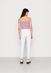 Top cropped com acabamento em ribana rosa e padrão quadriculado azul, combinado com jeans skinny brancos e sapatos de plataforma pretos. Vista traseira.