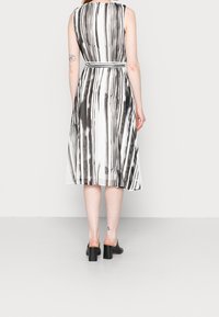 Schwarz-weiß gestreiftes ärmelloses Kleid mit tailliertem Schnitt und fließendem Rock, aus leichtem Stoff, kombiniert mit schwarzen Blockabsatzschuhen.