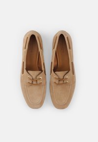 Beige semskede mokasiner med avrundet tå, utskjæringer på siden og dekorative snører med gyllen hardware. Glatt innersåle.