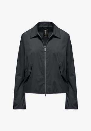 Giacca nera con zip e colletto, maniche lunghe, tasche anteriori inclinate e una piccola toppa sul braccio sinistro superiore, mostrata frontalmente su sfondo bianco.