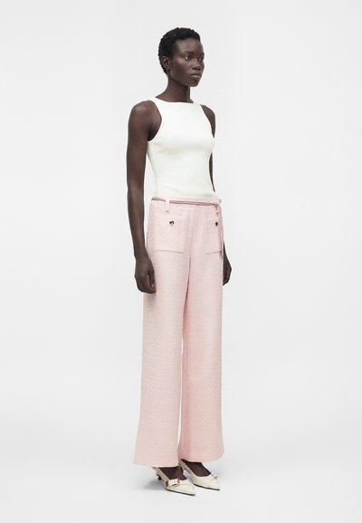 Μοντέλο φοράει λευκό αμάνικο τοπ, ροζ φαρδιά παντελόνια με μπροστινές τσέπες και κρεμ μυτερά τακούνια με λουράκια στον αστράγαλο.