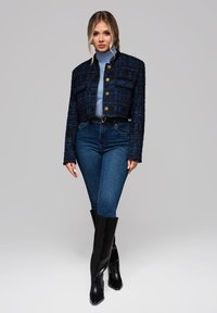 Kort navy tweedjacka med guldknappar, i kombination med ljusblå polotröja, mörkblå jeans och svarta knähöga klackstövlar.