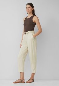 Bruine mouwloze top, crèmekleurige broek met een geweven riem en ronde gesp, en bruine sandalen met luipaardprintaccenten.