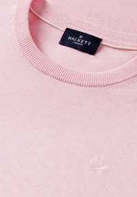 Maglione rosa chiaro con scollo a girocollo, collo a coste, piccolo logo ricamato sul petto e etichetta nera Hackett London all'interno del collo.