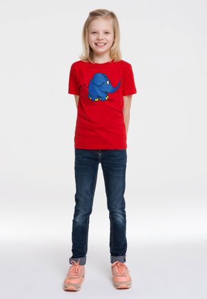 Red cotton t-shirt with a large blue elephant graphic, blue jeans, and light pink sneakers, standing against a white background.