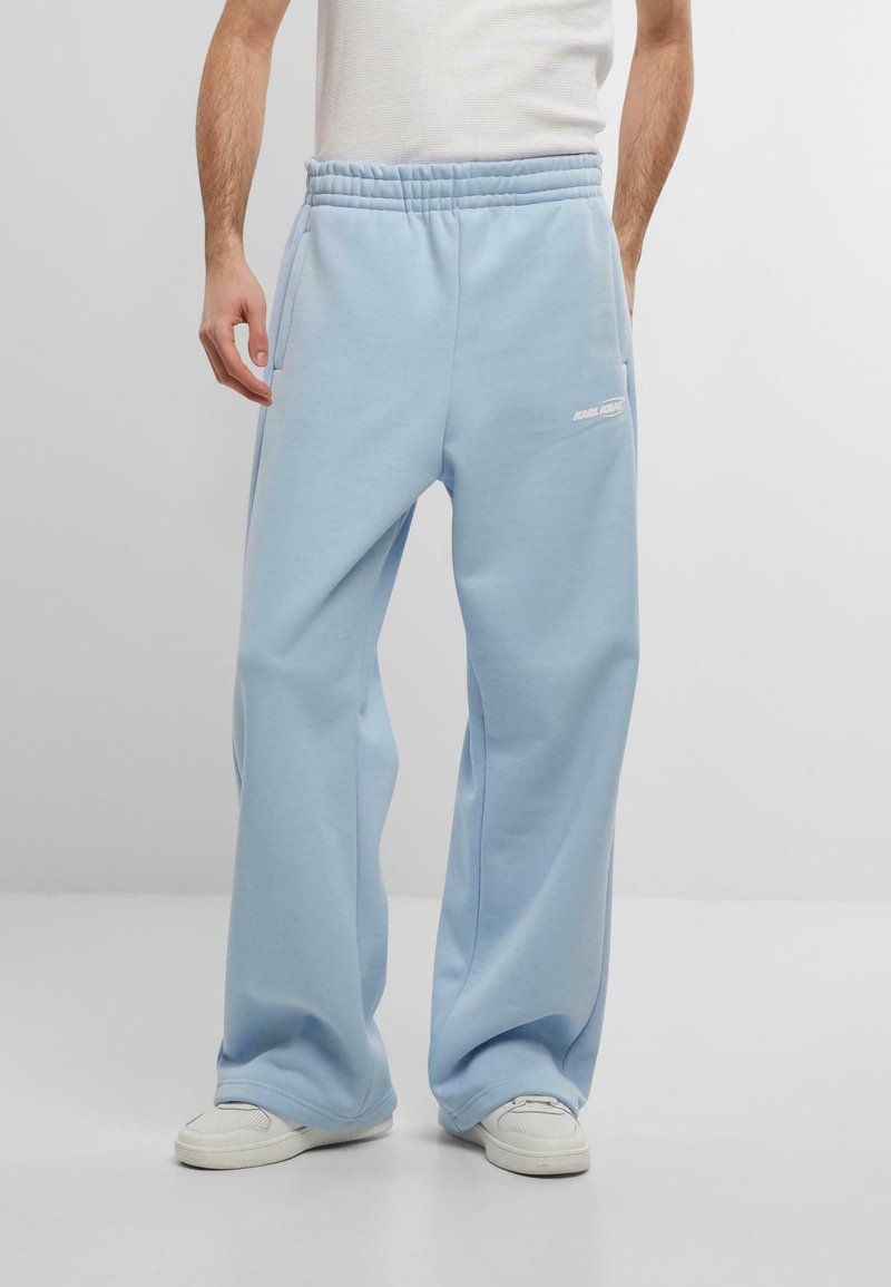 Light blue, loose-fitting sweatpants with an elastic waistband and side pockets. Features white logo text on the left thigh.
