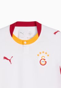 Λευκή αθλητική φανέλα με κόκκινο λογότυπο Puma στο δεξί στήθος και κόκκινο-κίτρινο έμβλημα της ομάδας με πέντε αστέρια στο αριστερό στήθος.