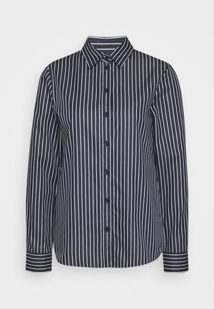 Chemise noire à manches longues et boutonnée, ornée de fines rayures verticales blanches, avec un col pointu et des poignets rayés, présentée sur un fond uni.