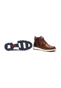 Botas de tobillo de cuero marrón con cremallera lateral, entresuela de color blanco roto y suela de goma texturizada en color navy. Presenta un diseño de cordones en la parte delantera y un acabado suave.