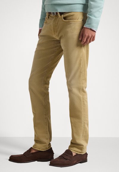 Απαλά μπεζ τζιν slim-fit με μαλακή υφή και ορατές ραφές. Συνδυάζονται με καφέ σουέτ μοκασίνια, αναδεικνύοντας μια casual εμφάνιση.