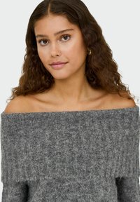 Pull gris décontracté à épaules dénudées avec une texture côtelée, un large décolleté et un matériau en tricot doux. Les manches évasées complètent le design.