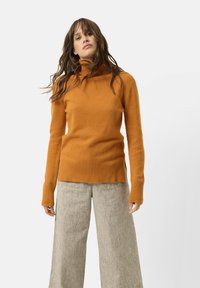 Oranžový rolák vyrobený z m ěkkého materiálu, s žebrovanými manžetami a spodním lemem. V kombinaci s béžovými kalhotami širokého střihu s texturovaným povrchem.