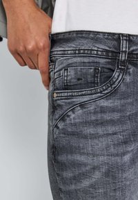 Jean en denim gris délavé avec un design à cinq poches, des détails de couture visibles et une coupe slim avec une légère texture usée.
