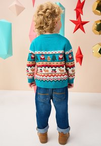 Tyrkysový pletený sveter s veselými vzormi, ktoré zobrazujú Santa Klausa, stromy a perníčky. Kombinovaný s modrými džínsami a hnedými topánkami.