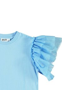 Ljusblå t-shirt med rundad halsringning och volangdetaljer i genomskinlig tyll på ärmarna. Tyget verkar slätt och mjukt.