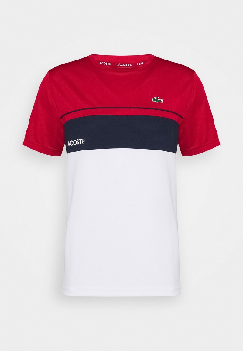 Punainen, laivastonsininen ja valkoinen väriblokkipaita, jossa on lyhyet hihat, pyöreä pääntie ja Lacosten logo rinnassa. Valmistettu pehmeästä kankaasta.