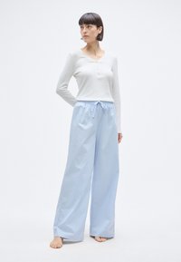 Φαρδύ παντελόνι ανοιχτού γαλάζιου χρώματος με ελαστική μέση και κορδόνι, σε συνδυασμό με λευκό μπλουζάκι henley μακρυμάνικο με κουμπιά.