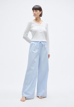 Šviesiai mėlynos plačios kelnės su elastinga juosmens dalimi ir raišteliu, derinamos su ilgomis rankovėmis baltais henley tipo marškinėliais su mygtukais.