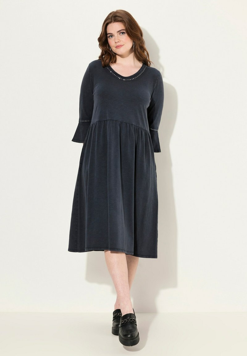 Czarna granatowa sukienka z okrągłym dekoltem, długimi rękawami i warstwową spódnicą. Zawiera subtelne metaliczne akcenty przy dekolcie i końcach rękawów.
