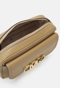 Tan leren handtas met gouden hardware, ritssluiting en een prominent MK-logo aan de voorkant. Het interieur heeft een bruine voering en een zak.