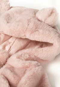 Tessuto morbido in peluche rosa chiaro con una texture soffice, caratterizzato da dettagli a forma di orecchie arrotondate e una fodera interna liscia, adatto per un indossare confortevole.