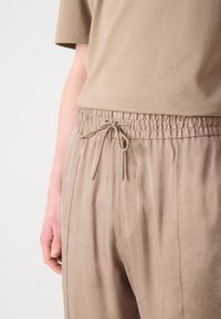 Pantalon en khaki avec taille élastique et cordon de serrage, présentant une texture douce comme du daim et des poches latérales ; associé à un haut à manches courtes assorti.