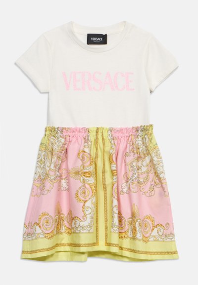 Λευκό φόρεμα με κοντά μανίκια και ροζ γράμματα "VERSACE" στο πάνω μέρος, και φούστα με πιέτες που παρουσιάζει ροζ, κίτρινα και χρυσά περίτεχνα μπαρόκ μοτίβα.