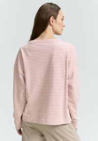 Maglietta a maniche lunghe di colore rosa chiaro con strisce orizzontali bianche, vestibilità morbida, scollatura rotonda e texture del tessuto morbida. Cuciture visibili sull'orlo.