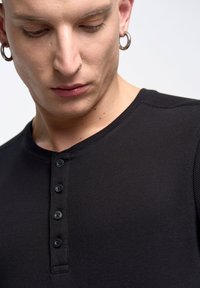 Černé žebrované tričko Henley s kulatým výstřihem a límcem na pět knoflíků. Materiál má texturovaný vzhled s jemnými švy.
