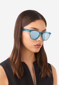 Gafas de sol azul aqua con lentes espejados, un diseño de montura elegante y una forma ligeramente puntiaguda. Presentan un logo en la patilla.