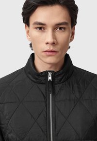 Czarna pikowana kurtka z wysokim kołnierzem, z przodem na zamek błyskawiczny, w diamentowy wzór i gładkiej fakturze. Minimalistyczny design i monochromatyczny kolor.