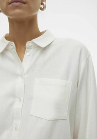 Valkoinen pellavapaita, jossa on kaulus, nappilista ja yksittäinen rintatasku. Pehmeä tekstuuri ja rento istuvuus.