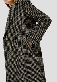 Dubbelzijdige zwart en beige houndstooth jas, met grote zwarte knopen en zijzakken. Gemaakt van textuurstof met een getailleerde pasvorm.
