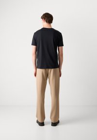 Tricou negru cu mânecă scurtă și guler rotund, asortat cu pantaloni bej, cu croială dreptă și pantofi negri. Design simplu, minimalist.
