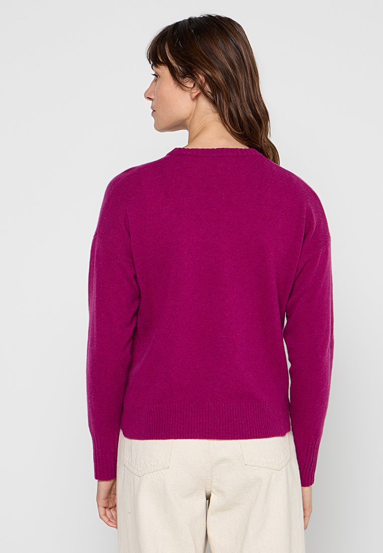 Magenta sweter z okrągłym dekoltem, z prążkowanymi mankietami i dołem. Miękka faktura i luźny krój, stylizowany z kremowymi spodniami.