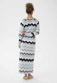 Robe à manches longues avec un motif en chevron dans des tons de bleu clair, crème et marine. Texture en maille avec une silhouette cintrée et des poignets élastiques. Coupe élancée.